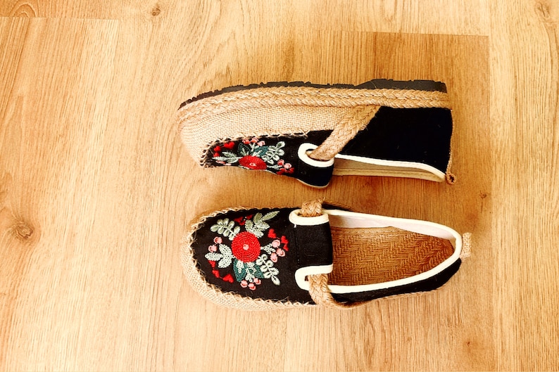 Op de afbeelding: Twee paar zwarte canvas schoenen met geborduurde bloemenmotieven. De schoenen hebben een jute zool en een witte rand rond de bovenkant.