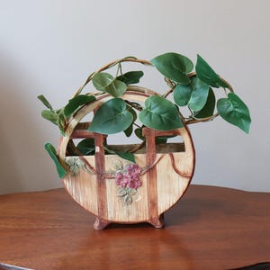 May include: A decorative ceramic planter with a brown and beige striped design and floral accents. The planter is shaped like a wheel and has a vine of green leaves growing out of it.