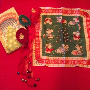 May include: A collection of Christmas-themed items on a red surface. Includes a vintage book titled "Christmas Joys", a green and red handkerchief with mice illustrations, and decorative ornaments with bells.