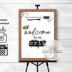 Può includere: Un cartello bianco stampabile con testo nero che recita "the notorious one" e "Welcome to my crib". Una corona gialla è sopra la parola "Welcome". Il cartello ha un design a spruzzo di vernice bianco e nero e una grafica solare in bianco e nero in basso con il testo "RAINE OF SUNSHINE".
