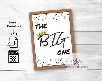 May include: A printable sign with a gold crown and the text "THE BIG ONE" in black script. The background is white with a confetti pattern of gold crowns, black lightning bolts, and black dashes.