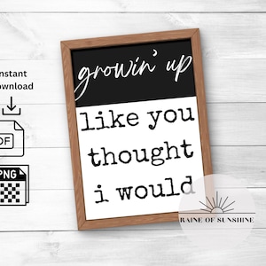 Può includere: Un cartello bianco e nero con il testo "growin' up like you thought i would". Il cartello è incorniciato da una cornice in legno nero e ha uno sfondo bianco. Il testo è in un font da macchina da scrivere.
