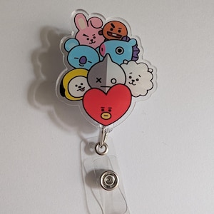 May include: A clear acrylic badge reel featuring a collection of colorful cartoon characters. The characters include a pink bunny, an orange face, a blue koala, a gray and white character, a yellow character, a white cloud, and a red heart.