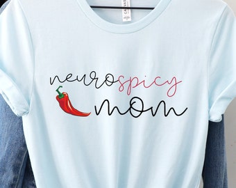Könnte beinhalten: Ein hellblaues T-Shirt mit dem Text "neurospicy mom" in schwarzer und rosa Schrift. Neben dem Text befindet sich eine rote Chilischote.