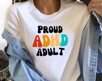 Könnte beinhalten: Weißes T-Shirt mit dem Text "PROUD ADHD ADULT" in bunten, Retro-Lettern.