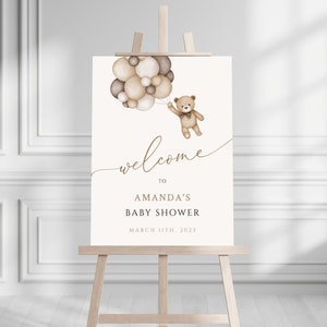 Puede incluir: Un cartel de bienvenida a la fiesta de bienvenida al bebé de Amanda con un oso de peluche marrón que sostiene un montón de globos marrones y blancos. El cartel dice "Bienvenido a la fiesta de bienvenida al bebé de Amanda 11 de marzo de 2023".