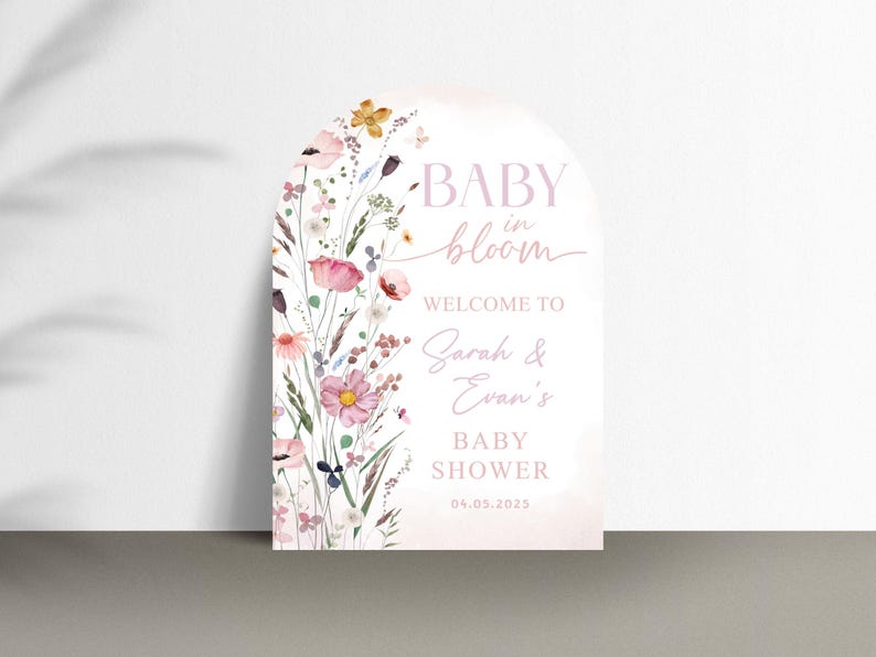 May include: A baby shower sign with a floral design. The sign is arched at the top and features the words "BABY in bloom" and "WELCOME TO Sarah & Evan's BABY SHOWER 04.03.2025". The sign is decorated with pink, yellow, and purple flowers.