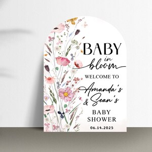 Puede incluir: Un cartel blanco en forma de arco con ilustraciones florales y el texto "BABY in bloom WELCOME TO Amanda's & Sean's BABY SHOWER 06.14.2025"