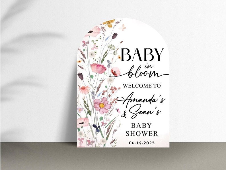 Puede incluir: Un cartel blanco en forma de arco con ilustraciones florales y el texto "BABY in bloom WELCOME TO Amanda's & Sean's BABY SHOWER 06.14.2025"