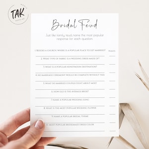 May include: Printable bridal shower game with the title "Bridal Feud". The game asks players to guess the most popular responses to wedding-related questions, such as "What type of fabric is a wedding dress made of?" and "What is the most popular wedding flower?"