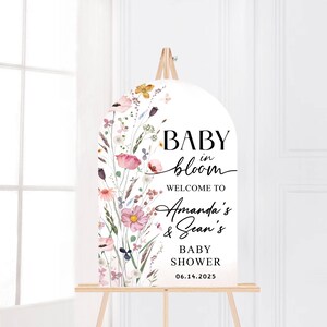 Puede incluir: Un cartel de bienvenida blanco con un dise&ntilde;o floral y el texto "Baby in bloom" con los nombres "Amanda's & Sean's" y la fecha "06.14.2025".