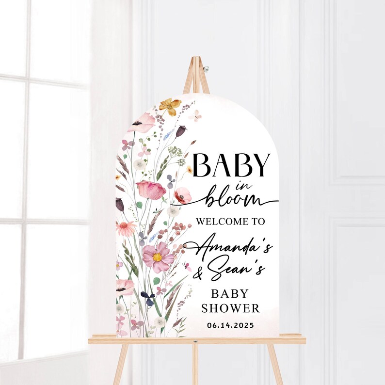Puede incluir: Un cartel de bienvenida blanco con un dise&ntilde;o floral y el texto "Baby in bloom" con los nombres "Amanda's & Sean's" y la fecha "06.14.2025".