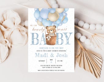 Può includere: Un invito per una festa di nascita con uno schema di colori blu e beige. L'invito presenta un orsacchiotto in un pallone aerostatico con il testo "We can barely wait BABY" e i nomi "Madi & Josh".
