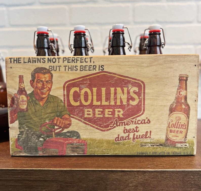 May include: Wooden beer carrier with six brown glass bottles. The carrier features a vintage-style graphic with the text "COLLIN'S BEER" and "America's best dad fuel!" The bottles have white and red stoppers.