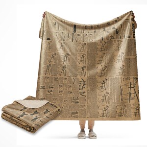 May include: A brown and beige throw blanket with a vintage newspaper print design. The blanket features black text and illustrations of tools and equipment. The blanket is folded and displayed on a white background.