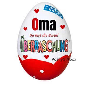 May include: A white chocolate egg with red hearts and the text "Oma Du bist die Beste!" and "&Uuml;BERRASCHUNG" in rainbow letters. The egg is wrapped in red foil with white polka dots.