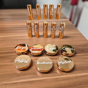 Pu&ograve; includere: Tubetti di rossetto dorati e contenitori rotondi con nomi personalizzati, tra cui "Astrid", "Brautinamar", "Marleew", "Birgit", "Martina", "Lea", "Carina", "Svenja", "Rebecca", "Angelina", "Julia", "Jemima", "Summer", "Daliya", "Adrienne" e "Julia".