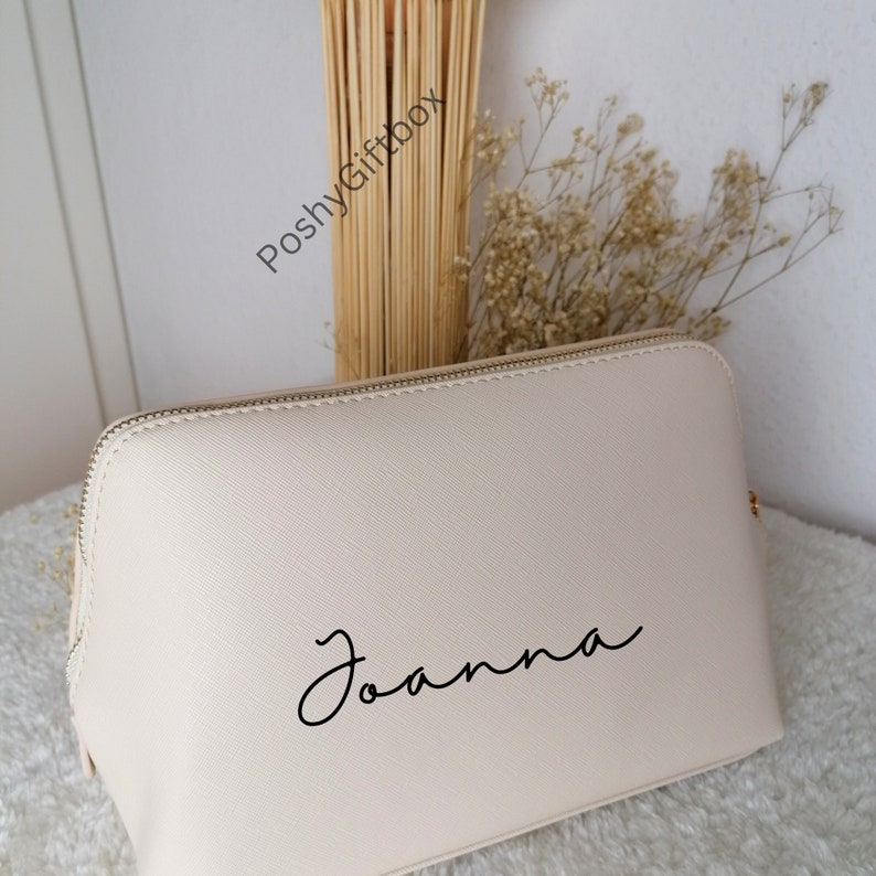 May include: A cream-colored zippered makeup bag with the name "Joanna" written in black cursive script.