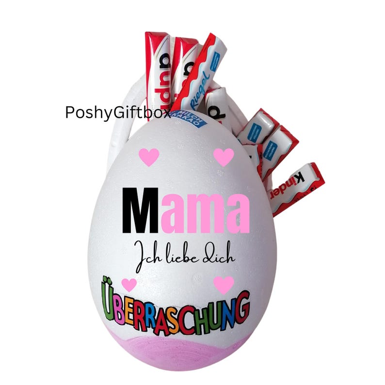 May include: A white egg-shaped gift box with the word "Mama" in black and pink, and the phrase "Ich liebe dich" below it. The word "&Uuml;berraschung" is at the bottom. The box is filled with candy bars.