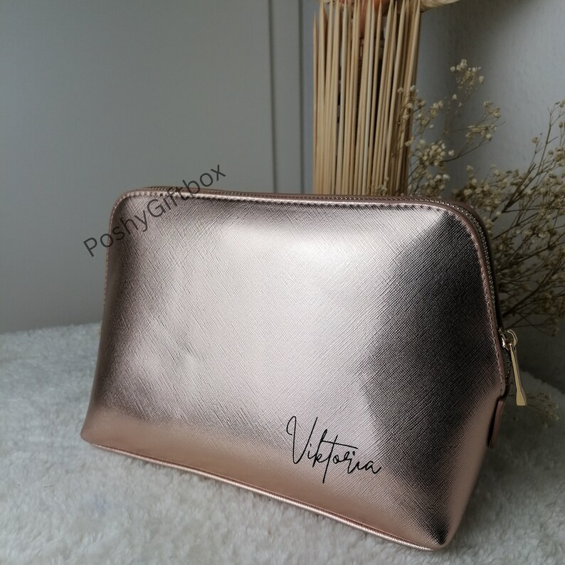 May include: A rose gold cosmetic bag with a zipper closure. The bag has the name "Viktoria" written on it in black.