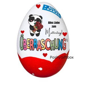 May include: A white chocolate egg with a red and white design. The egg has a panda bear holding a bouquet of red roses. The text on the egg says "Alles Liebe zum Muttertag!" and "&Uuml;BERRASCHUNG".