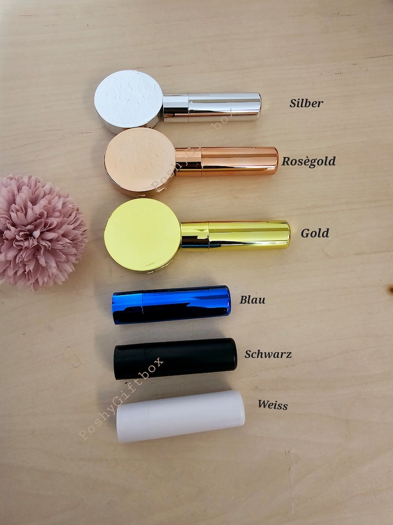 Pu&ograve; includere: Cinque tubetti di rossetto in diversi colori: argento, oro rosa, oro, blu e bianco. I tubetti sono disposti verticalmente, con il tubetto argentato in alto e il tubetto bianco in basso. Ogni tubetto ha un tappo rotondo e un'etichetta con il nome del colore in tedesco.