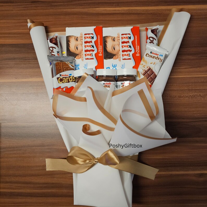 May include: A white gift box with a gold ribbon tied in a bow. The box is filled with various chocolate bars and spreads, including Kinder chocolate, Nutella, and Kinder Country. The box is labeled "Poshy Giftbox".