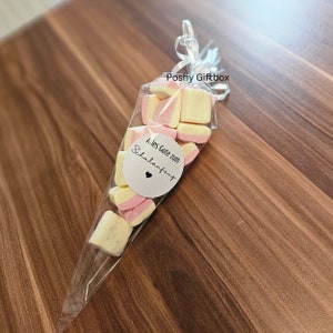 May include: A clear plastic cone filled with pink and yellow marshmallows. A white circle sticker with the text "Alles Gute zum Schulanfang" and a small heart is attached to the cone.