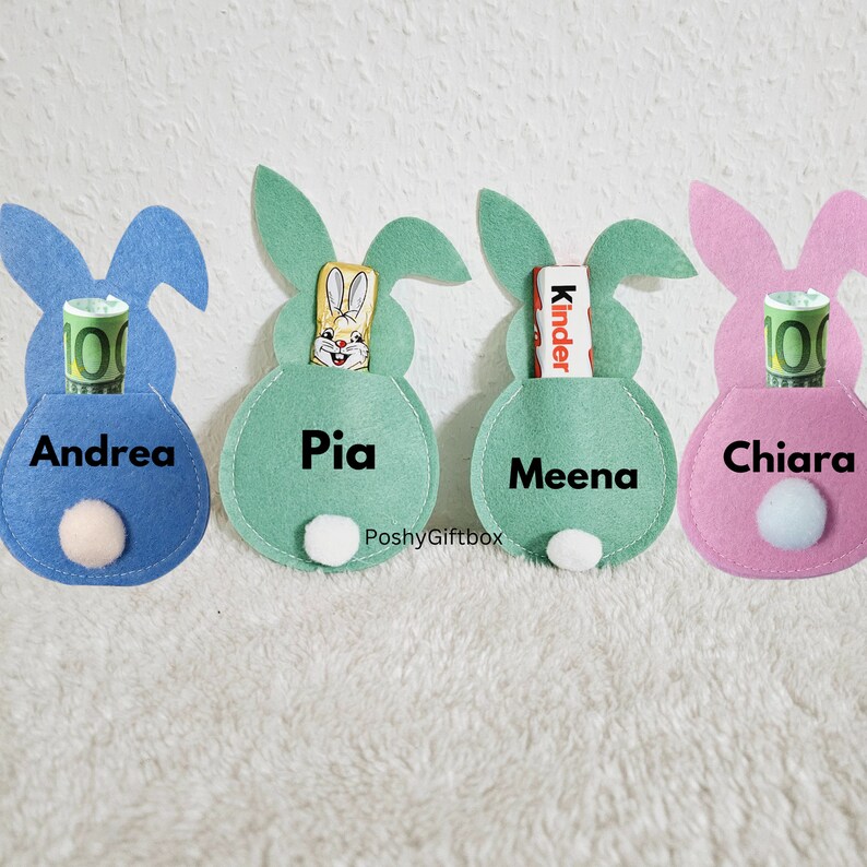 May include: Four felt Easter bunny gift bags with names Andrea, Pia, Meena, and Chiara. Each bag has a different treat inside: money, a chocolate bar, and a Kinder chocolate bar.