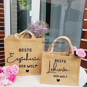 May include: Two brown burlap tote bags with black text. The larger bag says "Beste Erzieherin der Welt" and the smaller bag says "Beste Lehrerin der Welt". Both bags have a small black heart at the bottom.