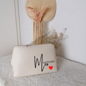 May include: A cream-colored cosmetic bag with a black cursive "Mrs. Fletcher" design and a red heart.