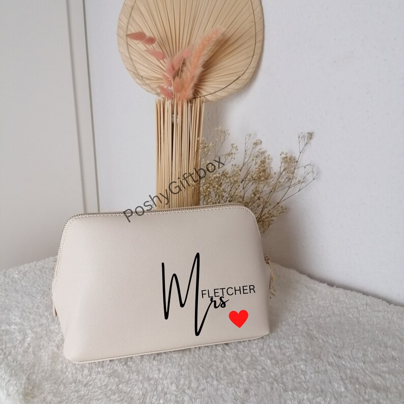 May include: A cream-colored cosmetic bag with a black cursive "Mrs. Fletcher" design and a red heart.
