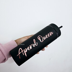 May include: Black reusable tumbler with a rose gold inscription that reads "Aperol Queen".