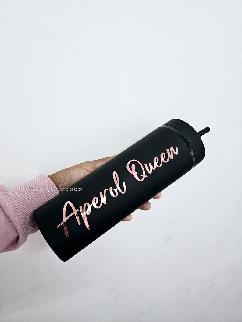 May include: Black reusable tumbler with a rose gold inscription that reads "Aperol Queen".