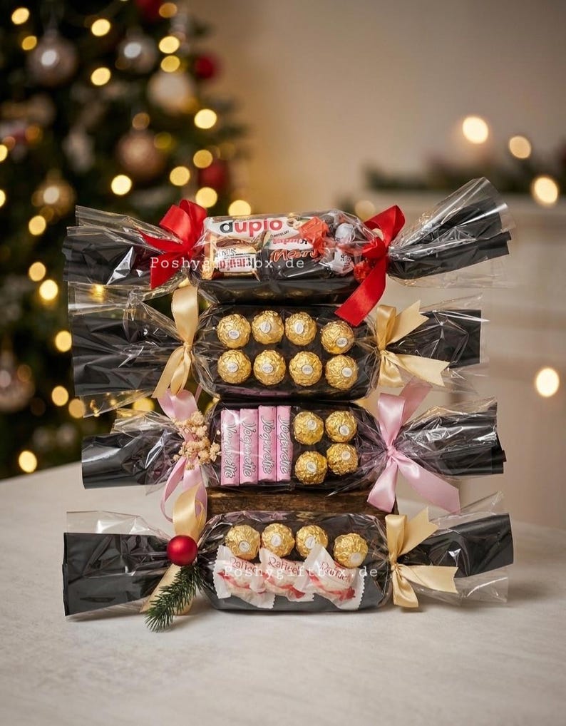 May include: A stack of four gift-wrapped candy packages in clear cellophane with black paper inserts. Each package is tied with ribbons in red, gold, or pink. The contents include various chocolate bars and gold-foiled round candies.