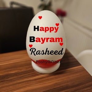 May include: White styrofoam egg with red hearts and black text that reads "Happy Bayram Rasheed" and "PoshyGiftbox".