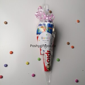 May include: A clear plastic cone filled with assorted chocolate bars and candies. A white sticker with the text "Danke f&uuml;r die tolle Zeit" and a star is attached to the cone. The cone is tied with a pink ribbon.