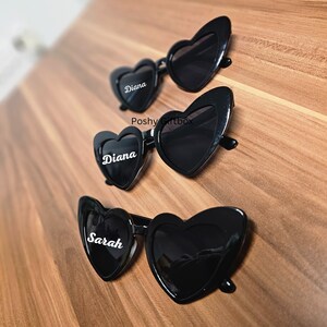 May include: Three pairs of black heart-shaped sunglasses with the names "Diana" and "Sarah" written on them.