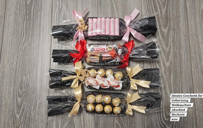 May include: Four candy gift crackers wrapped in black cellophane with clear plastic, tied with pink, red, and gold ribbons. Each contains assorted chocolates and sweets, including pink wafer sticks, Duplo, Ferrero Rocher, and Raffaello candies.