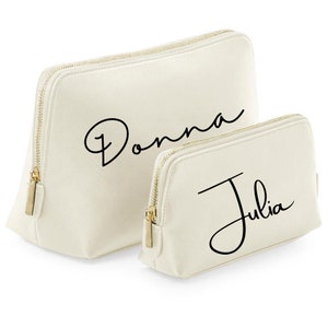 May include: Two off-white zippered cosmetic bags with gold zippers. The larger bag has the name "Donna" written in black cursive script. The smaller bag has the name "Julia" written in black cursive script.