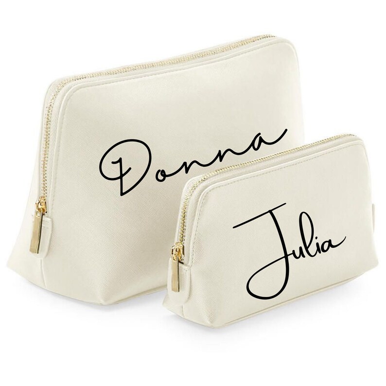 May include: Two off-white zippered cosmetic bags with gold zippers. The larger bag has the name "Donna" written in black cursive script. The smaller bag has the name "Julia" written in black cursive script.