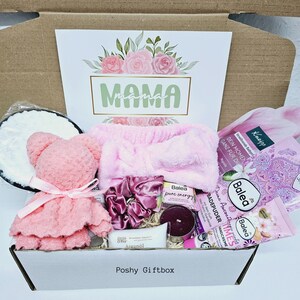 Peut inclure: Une bo&icirc;te cadeau rose remplie de produits de bain et de corps, dont un bandeau rose, un ours en peluche rose, une bougie et une bouteille de lotion. La bo&icirc;te est &eacute;tiquet&eacute;e "Poshy Giftbox" et porte une carte avec le mot "MAMA" dessus.