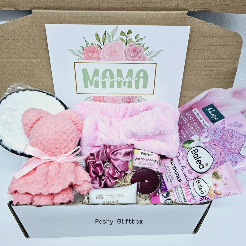 Peut inclure: Une bo&icirc;te cadeau rose remplie de produits de bain et de corps, dont un bandeau rose, un ours en peluche rose, une bougie et une bouteille de lotion. La bo&icirc;te est &eacute;tiquet&eacute;e "Poshy Giftbox" et porte une carte avec le mot "MAMA" dessus.