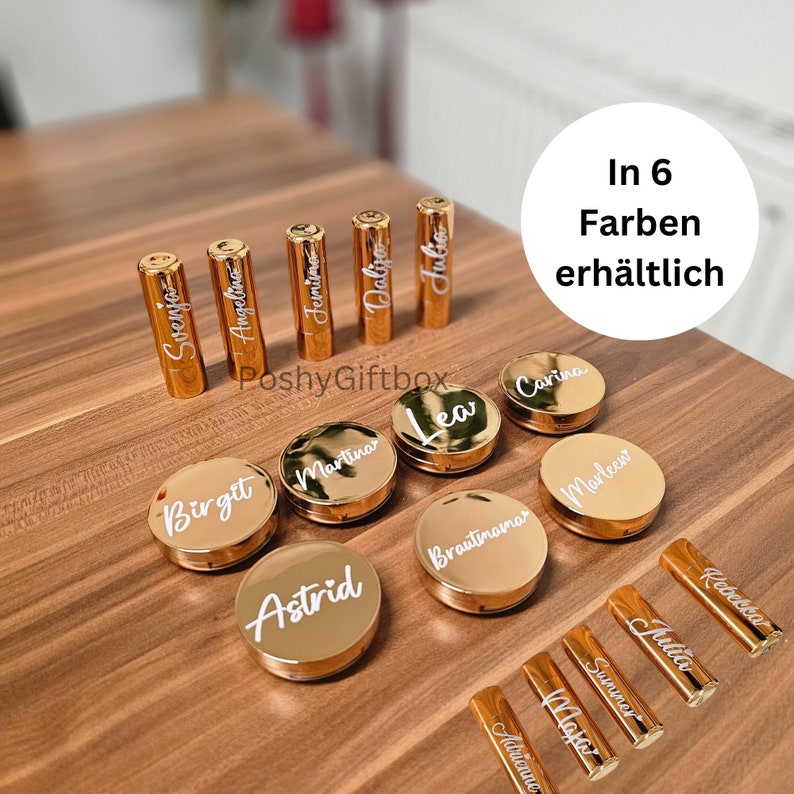 Pu&ograve; includere: Tubetti di rossetto dorati e contenitori rotondi con nomi personalizzati in lettere bianche. Il testo "In 6 Farben erh&auml;ltlich" &egrave; visibile nell'angolo in alto a destra dell'immagine.
