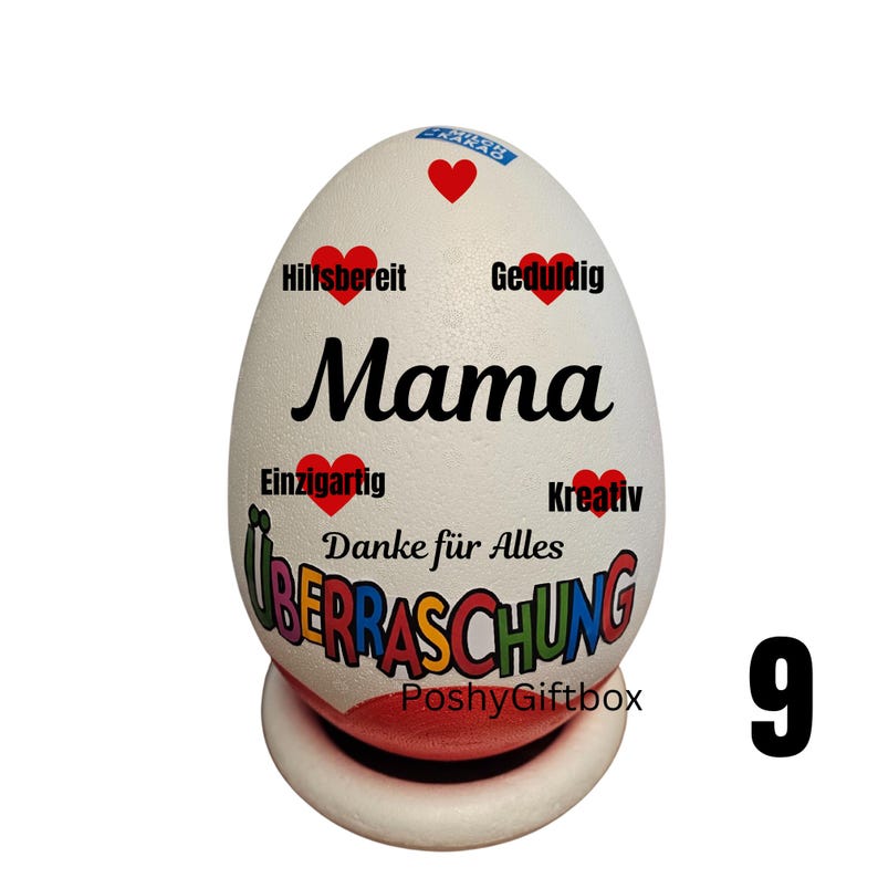 May include: A white egg-shaped decorative item with the word "Mama" in black script. It features red heart accents and German words like "Hilfsbereit" and "&Uuml;berraschung". The egg rests on a white and red base.