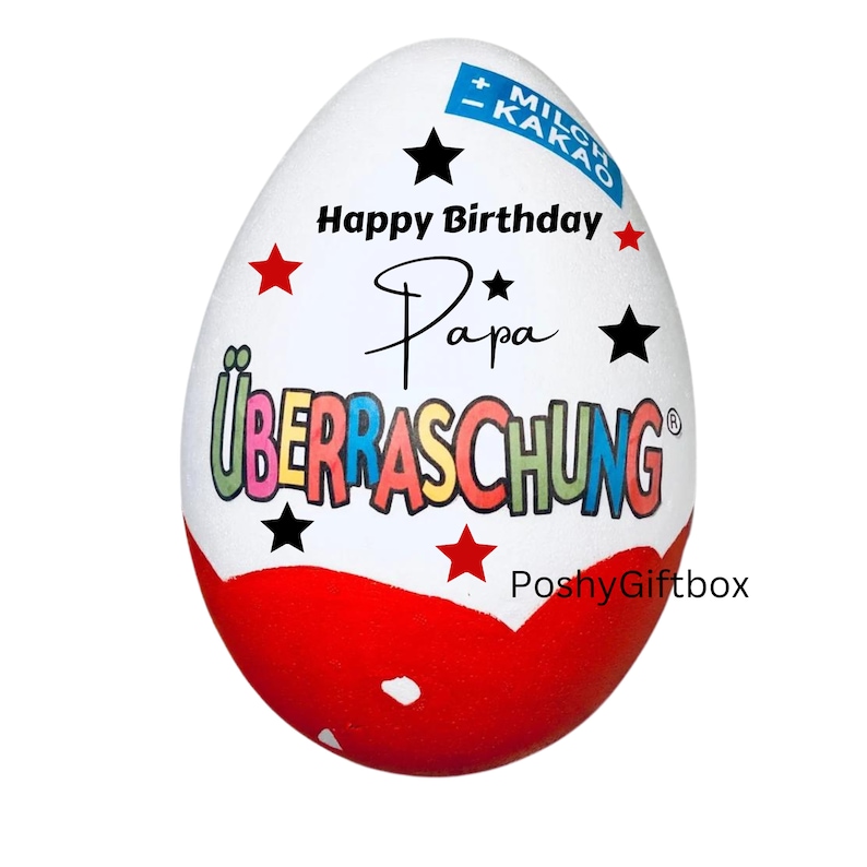 May include: A white chocolate egg with a red, white, and blue design. The egg has the words "Happy Birthday Papa" and "Ueberraschung" written on it. The egg is decorated with red and black stars.