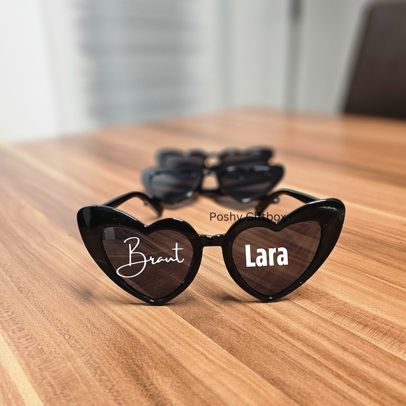 May include: Two pairs of black heart-shaped sunglasses with white text. The sunglasses on the bottom say "Brant" and "Lara".
