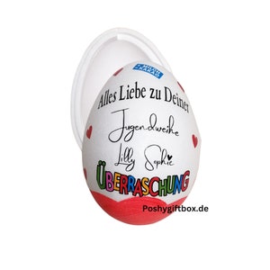 May include: A white egg-shaped container with a red base and a clear lid. The egg is decorated with red hearts and black script that reads "Alles Liebe zu Deiner Jugendweihe Lilly Sophie &Uuml;BERRASCHUNG". The container has a "Milch Kakao" logo.