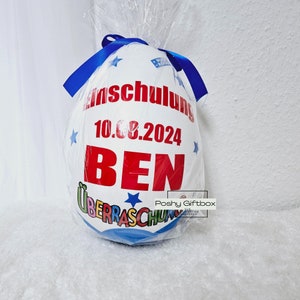 Peut inclure: Un ballon blanc en forme d'&oelig;uf avec un ruban bleu, d&eacute;cor&eacute; d'&eacute;toiles et du texte "Einschulung 10.08.2024 BEN &Uuml;berraschung".