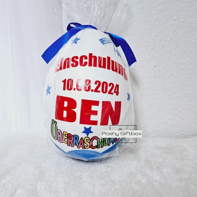 Peut inclure: Un ballon blanc en forme d'&oelig;uf avec un ruban bleu, d&eacute;cor&eacute; d'&eacute;toiles et du texte "Einschulung 10.08.2024 BEN &Uuml;berraschung".